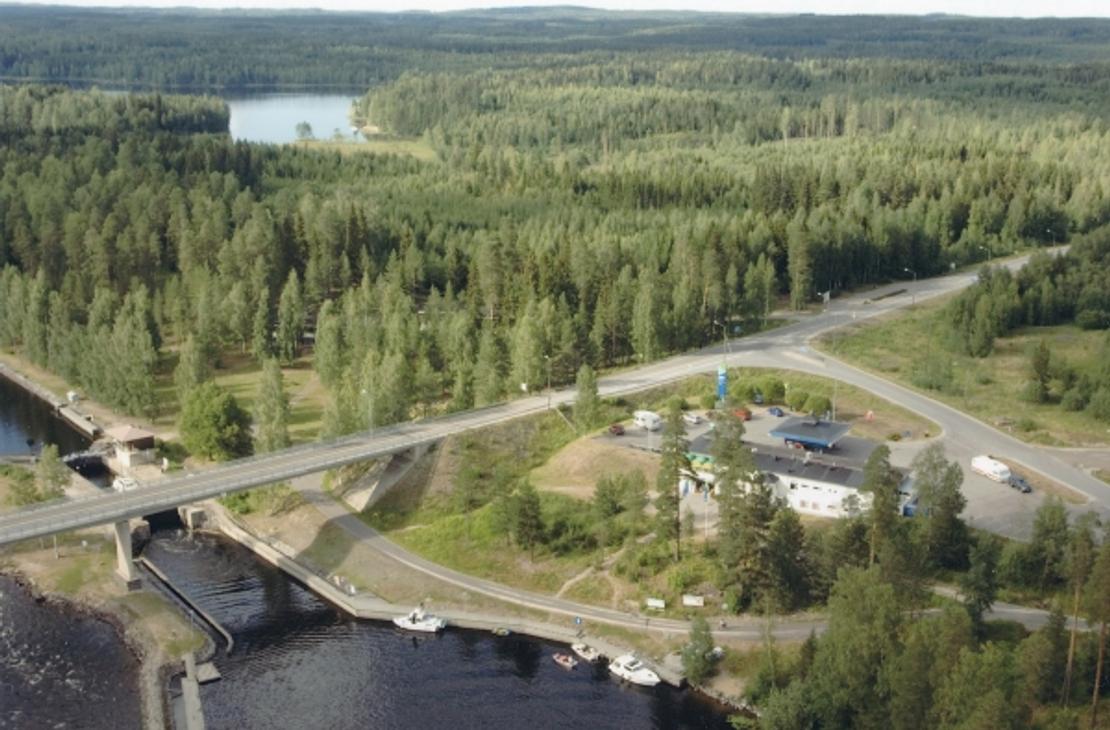 Ilmakuva Karvion kanavalta, jossa valtatie 23 ylitt&auml;&auml; kanavan siltaa pitkin. Kuvassa n&auml;kyy etualalla kanavan sulkuportteja ja laitureihin kiinnitettyj&auml; veneit&auml;. Tien vieress&auml; sijaitsee Neste Karvionkanava -huoltoasema rakennuksineen ja parkkialueineen. Taustalla avautuu laaja ja vehre&auml; mets&auml;maisema sek&auml; kaukana siint&auml;v&auml; vesist&ouml;.