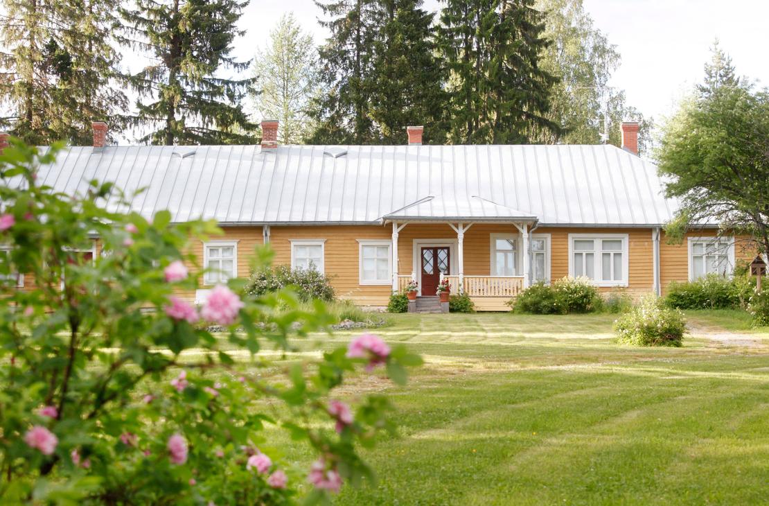 Möhkön ruukkimuseon pitkä, keltainen puurakennus, jonka edessä on laaja nurmikko ja kukkivia pensasruusuja. Rakennuksessa on valkoiset ikkunankarmit, harmaa peltikatto ja pieni katettu kuisti.