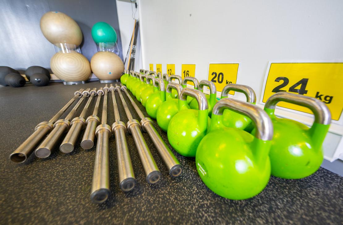 L&auml;hikuva Kinesiocenter Kuntoilukeskuksen kuntosaliv&auml;lineist&auml; lattialla. Etualalla riviss&auml; on useita kirkkaan limevihreit&auml; kahvakuulia hopeanv&auml;risill&auml; kahvoilla. Niiden vasemmalla puolella on rivi lyhyit&auml;, metallisia painonnostotankoja. Taustalla n&auml;kyy sein&auml;&auml; vasten pino suuria, beigenv&auml;risi&auml; jumppapalloja. Oikealla sein&auml;ll&auml; on keltaisia merkint&ouml;j&auml; painoista, kuten "20 kg" ja "24 kg".