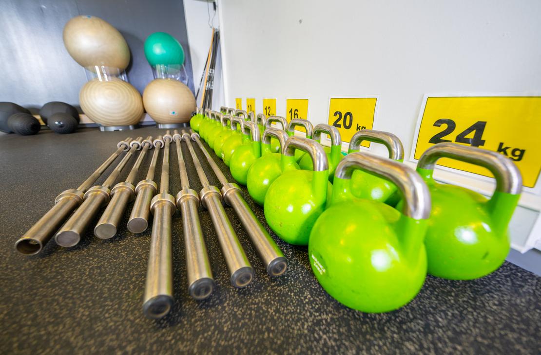 L&auml;hikuva Kinesiocenter Kuntoilukeskuksen kuntosaliv&auml;lineist&auml; lattialla. Etualalla riviss&auml; on useita kirkkaan limevihreit&auml; kahvakuulia hopeanv&auml;risill&auml; kahvoilla. Niiden vasemmalla puolella on rivi lyhyit&auml;, metallisia painonnostotankoja. Taustalla n&auml;kyy sein&auml;&auml; vasten pino suuria, beigenv&auml;risi&auml; jumppapalloja. Oikealla sein&auml;ll&auml; on keltaisia merkint&ouml;j&auml; painoista, kuten "20 kg" ja "24 kg".