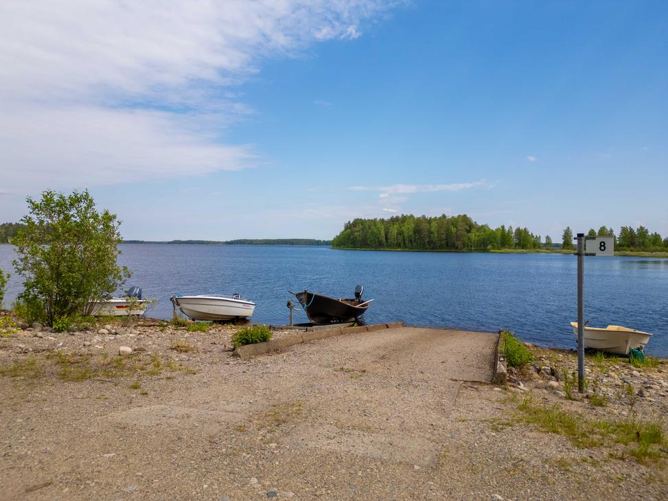 Näkymä sorapäällysteiseltä veneenlaskupaikalta järvelle. Rannassa on betonisluiska, muutamia pienveneitä sekä opastepylväs, jossa on numero 8.