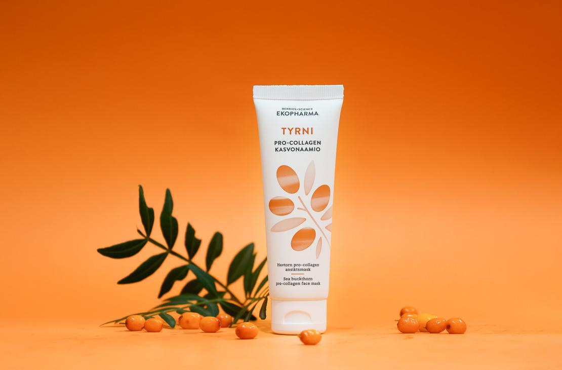 Ekopharma Tyrni Pro-Collagen -kasvonaamiotuubi oranssilla taustalla. Tuubin vieress&auml; on vihre&auml; tyrninoksa ja muutama tyrnimarja oranssilla alustalla.