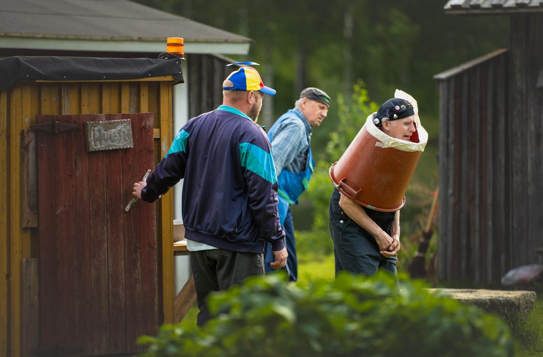 M&ouml;hk&ouml;n kes&auml;teatterin Peitetarina-n&auml;ytelm&auml;n kohtaus, jossa kolme miest&auml; esiintyy ulkon&auml;ytt&auml;m&ouml;ll&auml;. Vasemmalla mies, jolla on v&auml;rik&auml;s potkurilippis, on avaamassa puisen ulkok&auml;ym&auml;l&auml;n ovea, jossa on teksti "Huussi". Oikealla vanhempi mies seisoo vartalonsa ymp&auml;rille asetetun suuren ruskean muovisaavin sis&auml;ll&auml; ilmehtien vaivautuneesti, ja heid&auml;n takanaan kolmas mies seuraa tilannetta.