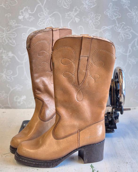 Pari klassisia, vaaleanruskeita nahkasaappaita, joissa on koristeellisia tikkauksia varressa ja maltillinen koro.